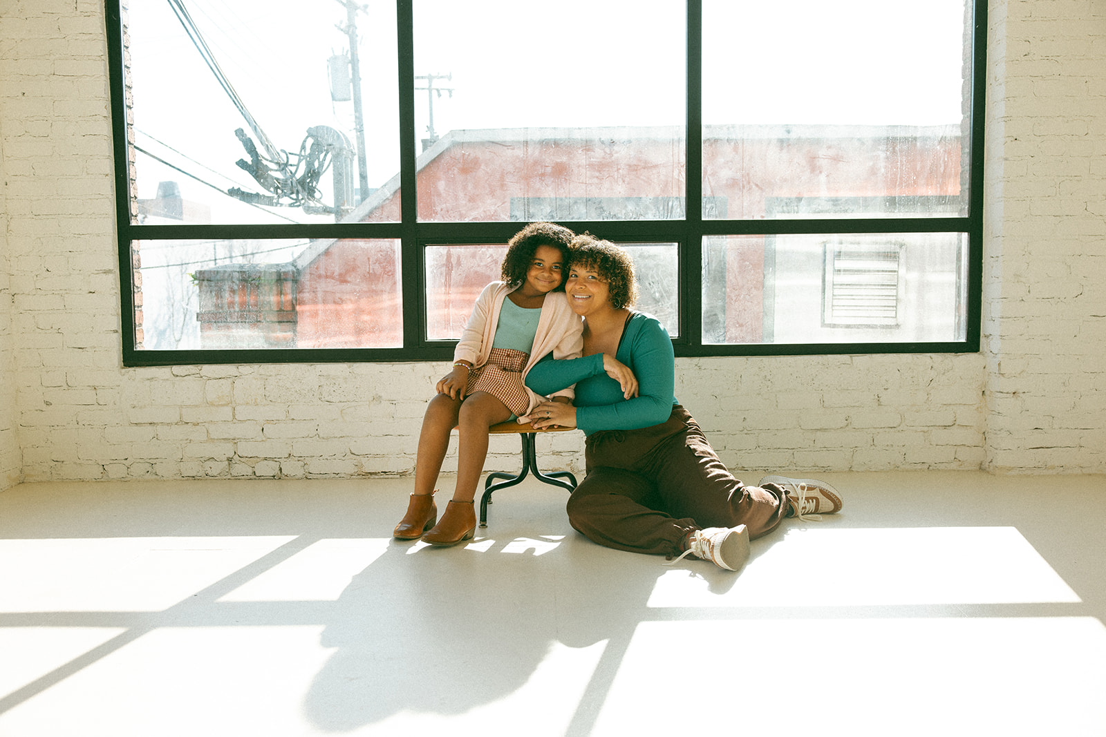 black girl sitting on vintage chair in minimalist studio with mom sitting on floor next to her