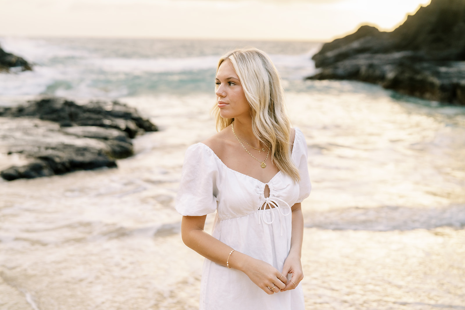 high school senior portrait of a woman in a white dress standing by the seaside at sunrise at Halona Cove