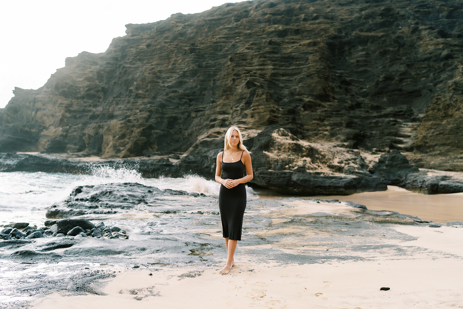 Woman standing on a beach with rocky outcrops, captured by Hawaii senior portrait photographer Megan Moura