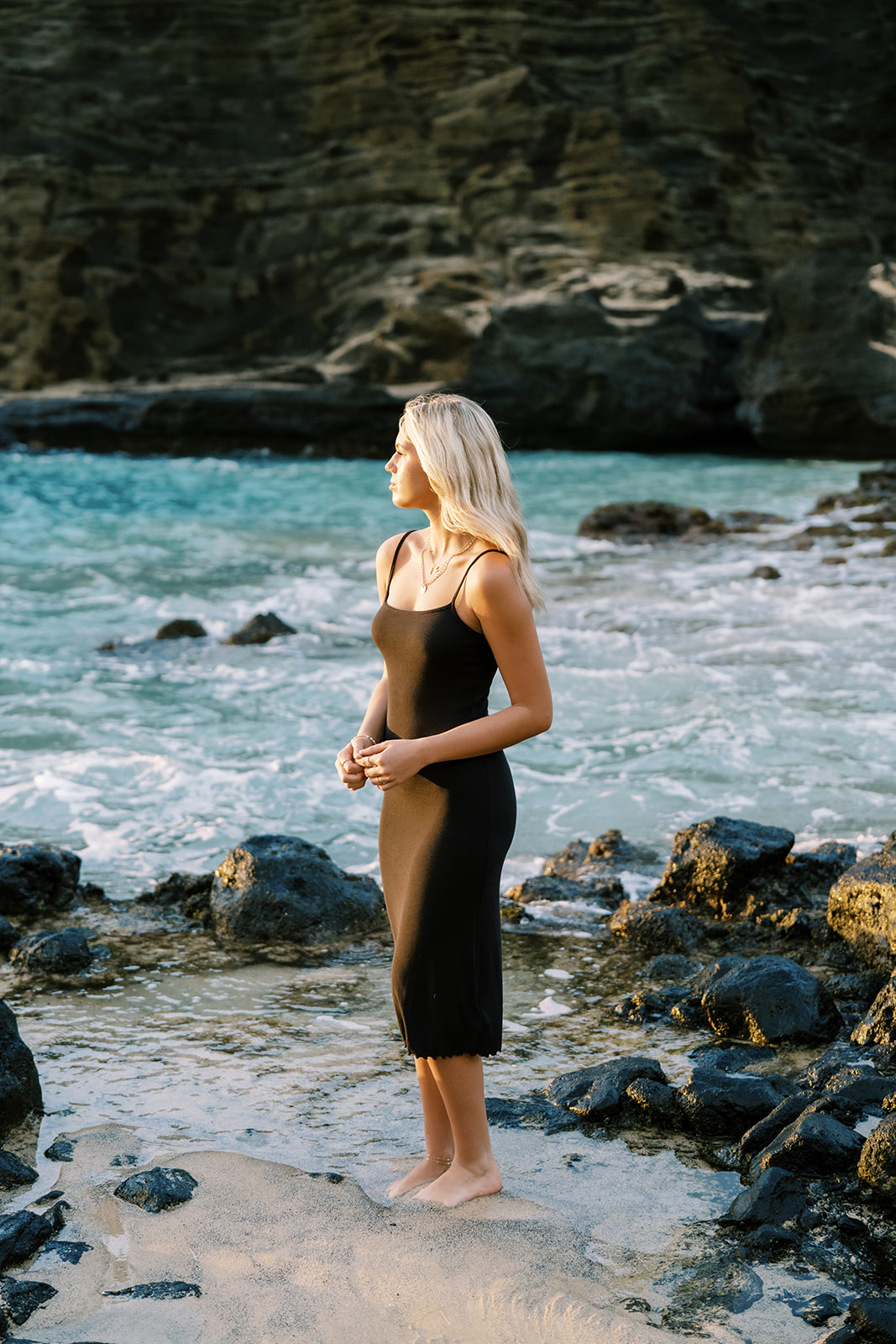 A woman standing on a rocky shore by the sea, looking into the distance high school senior portrait at Halona Cove