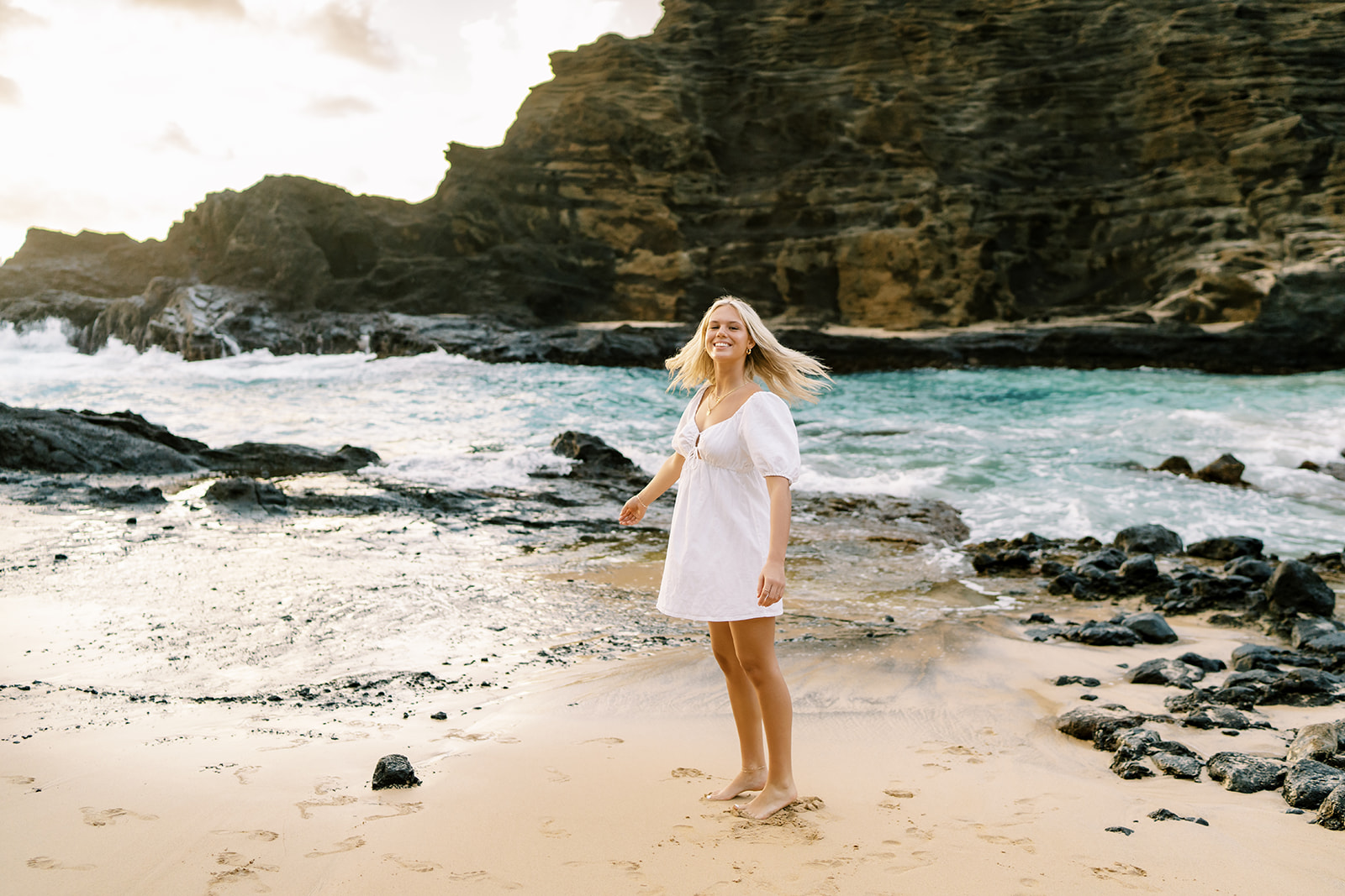 A high school senior in a white dress playing around by herself at Halona Cove in Oahu