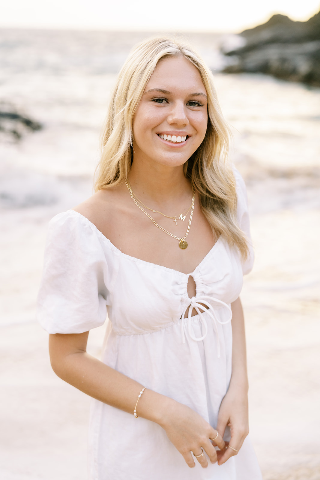 A smiling young woman in a white dress standing on Halona Cove beach in Oahu