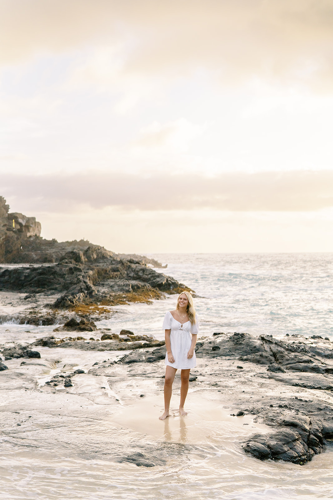 Woman standing on a rocky shoreline at sunset captured by Hawaii senior portrait photographer Megan Moura