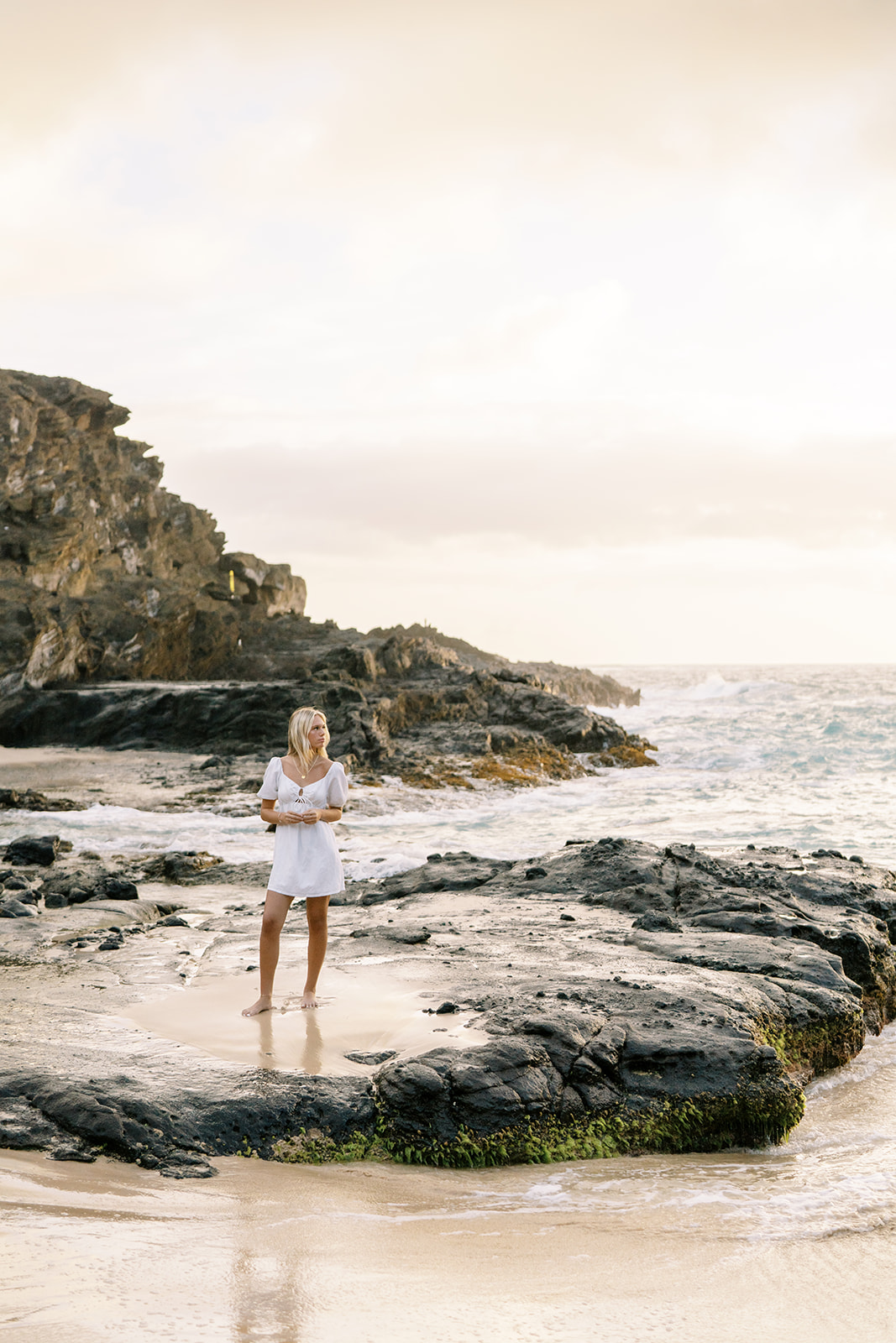 A woman standing on a rocky shore by the sea during her high school senior portrait session at Halona Cove