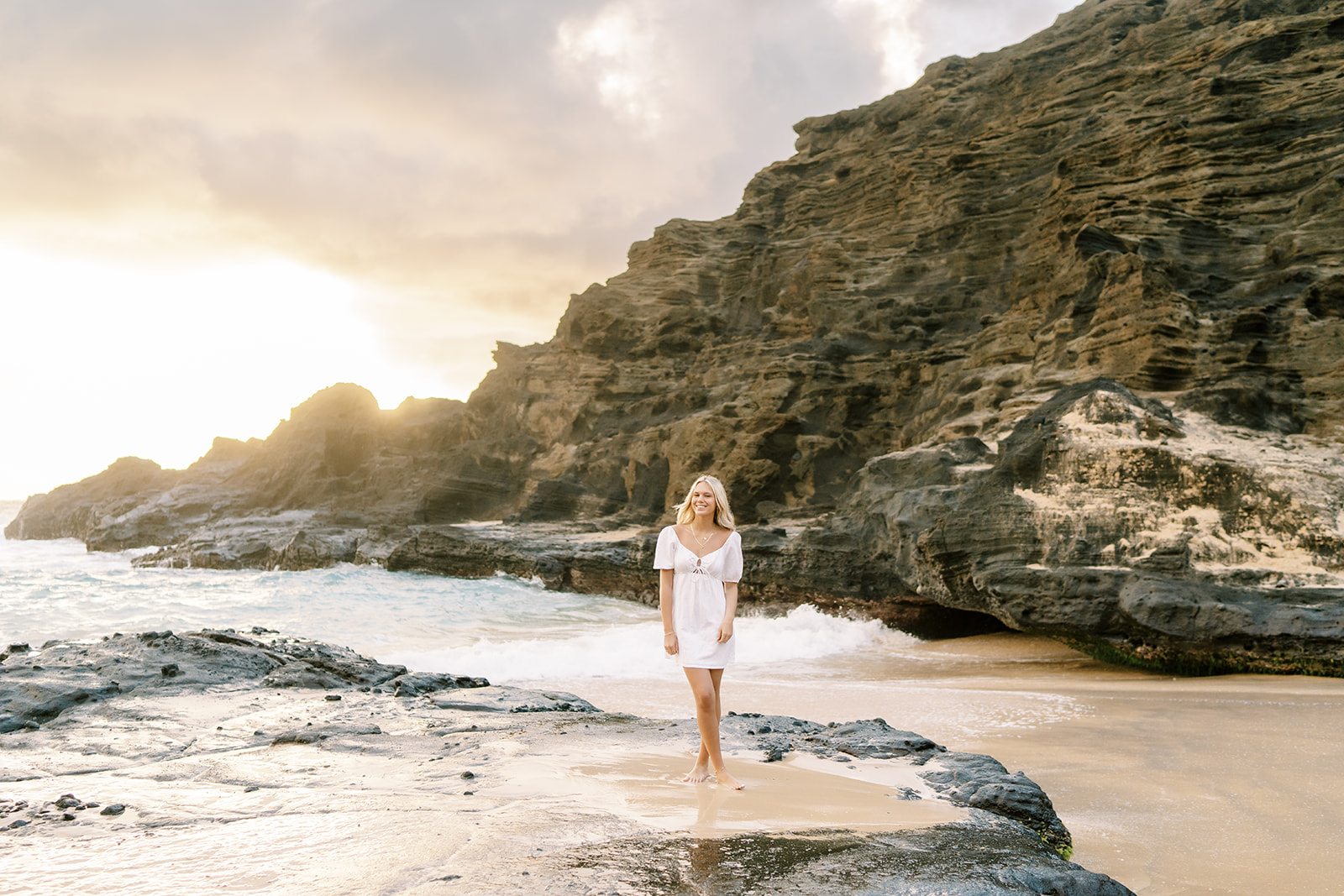 Woman standing on a rocky beach enjoying the sunrise during her Sunrise High School Portrait Session 