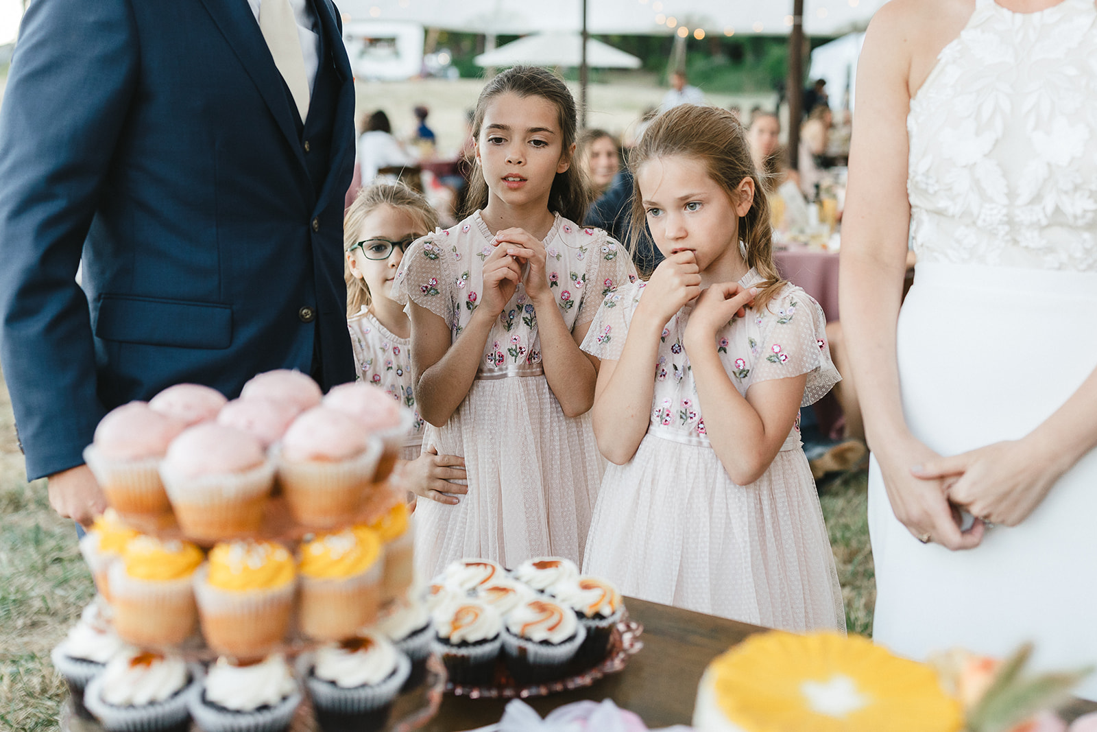 Flower girls looking at a dessert table full of cupcakes and sweets.