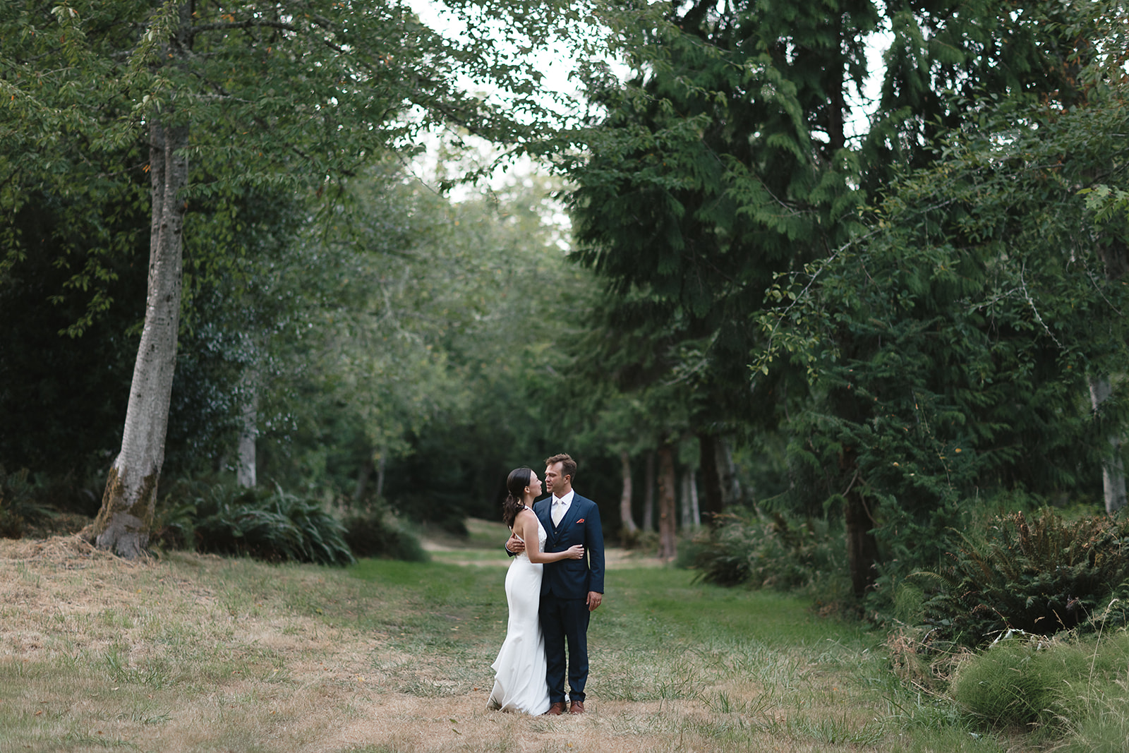Wide angle view of a bride and groom in front of a row of trees at Vashon Field and Pond venue.
