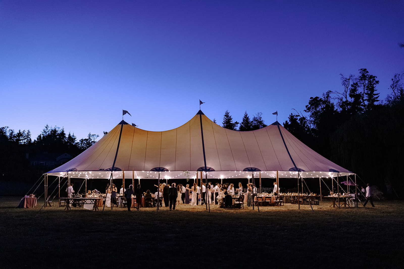 Wide angle view of a reception tent at a wedding at dusk.