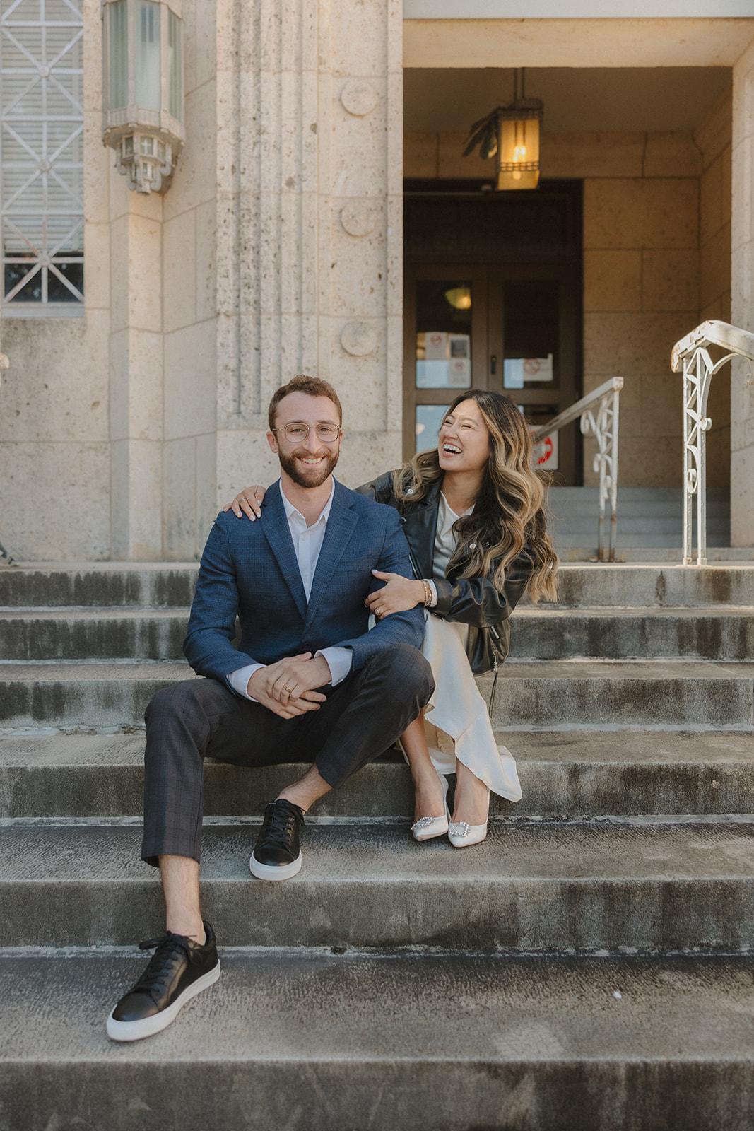 bride and groom laughing and sitting on the steps outside of the courthouse after their elopement in downtown Austin 