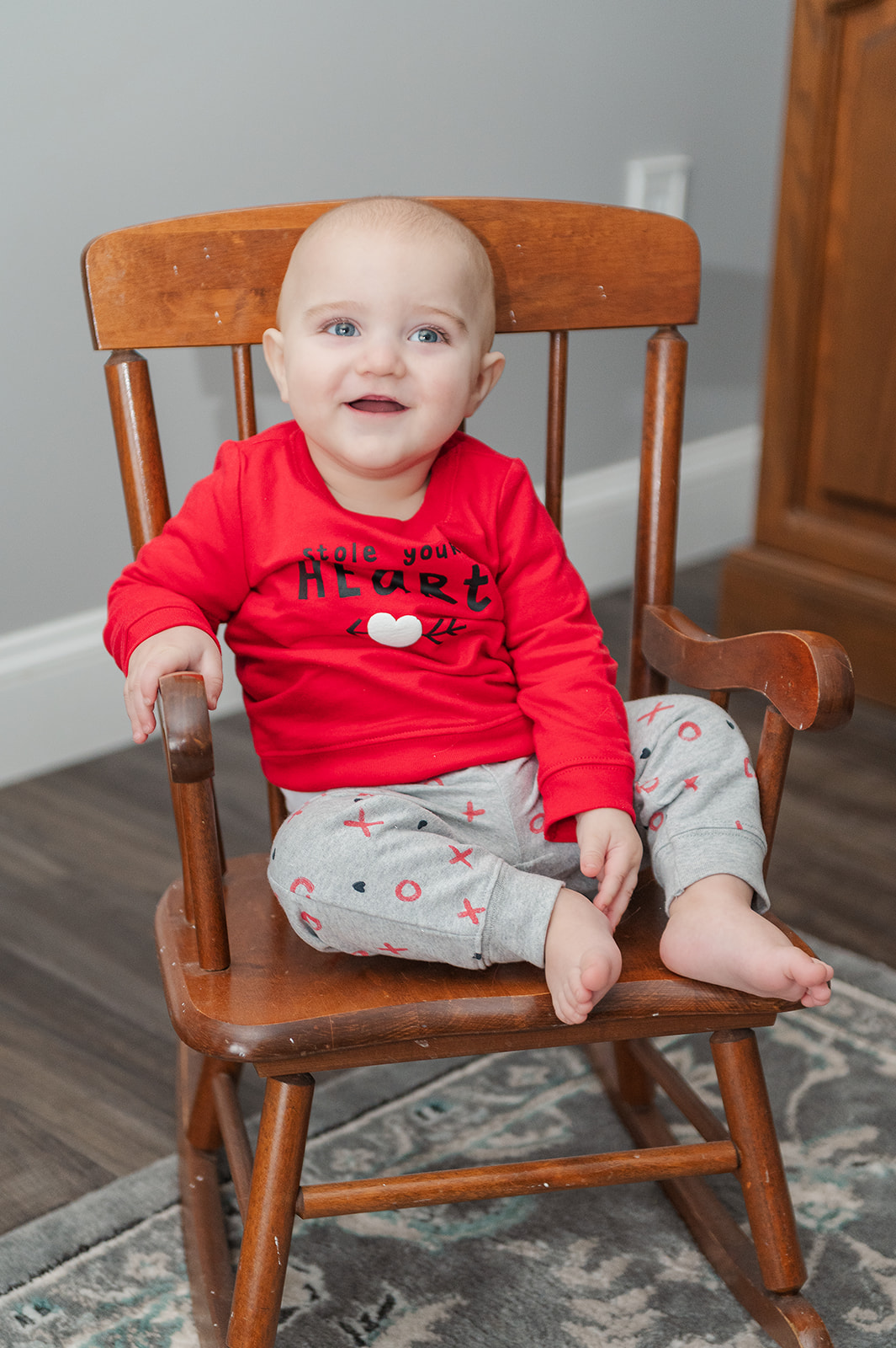 9 month old sitting on small wood rocking chair wearing a valentine's day outfit