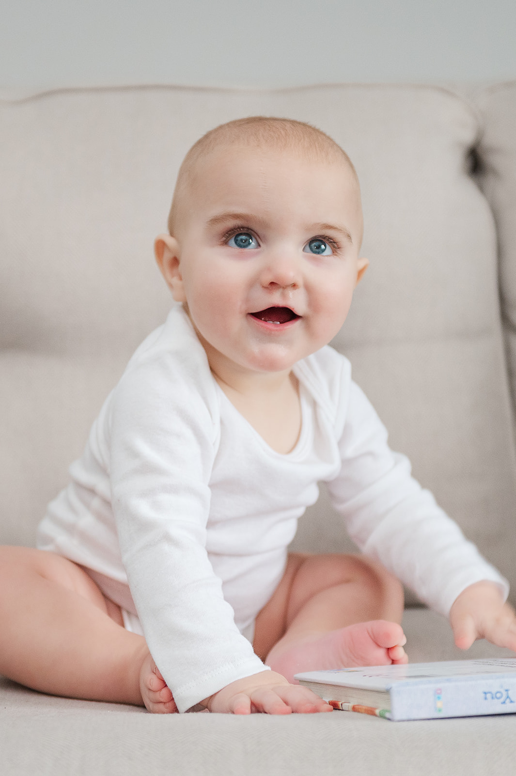 9 month old sitting on the couch with a sweet smile and big blue eyes