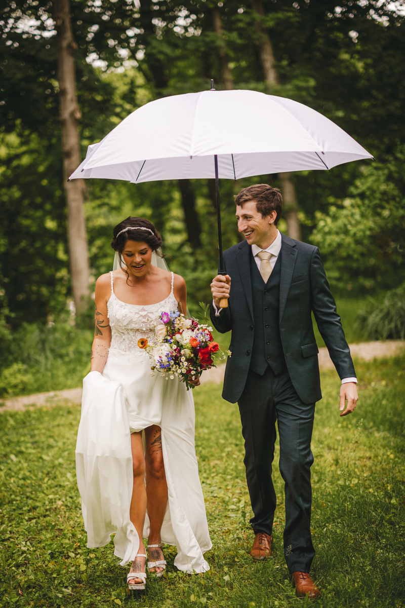 a groom holds an umbrella for his bride as they walk to their  Berkshires wedding 