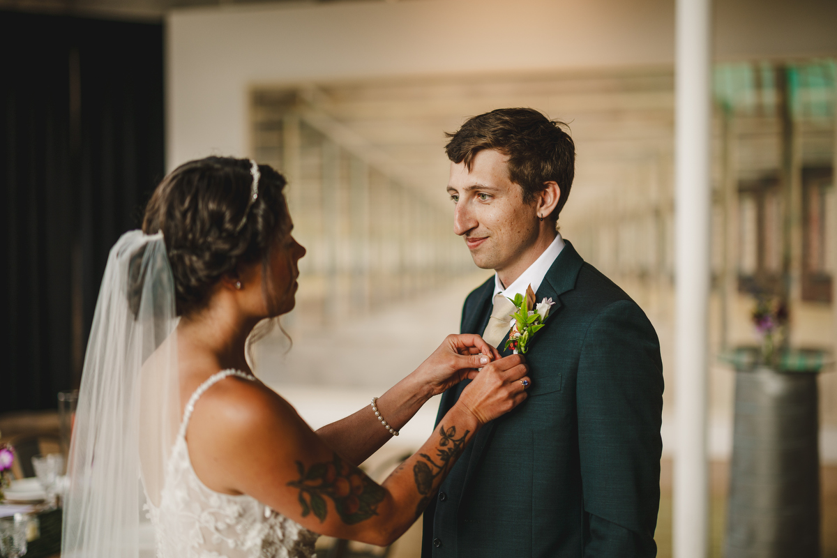 Bride fixes her groom's boutonniere before their wedding at MASS MoCA 