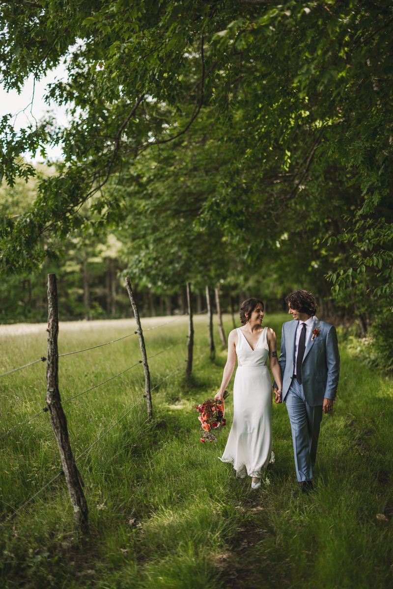 smiling bride and groom walk along a fence and horse pasture at valley view farm 
