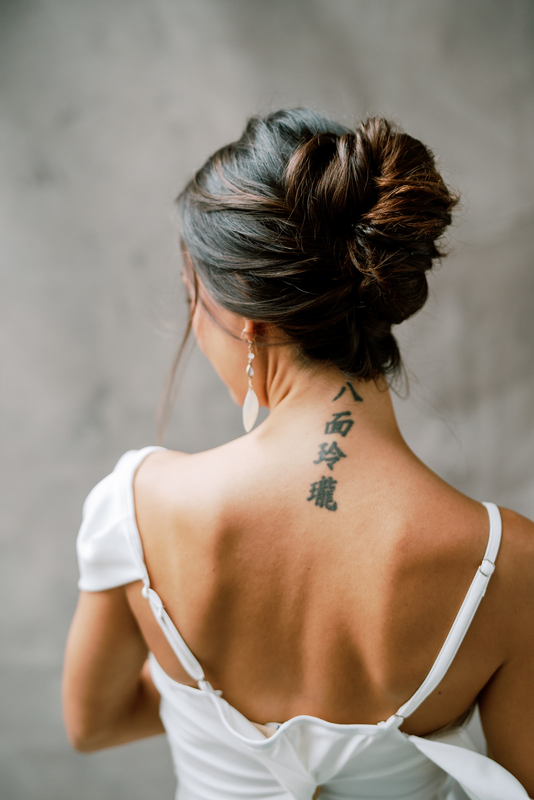 A woman with her hair tied up high and a chinese tattoo on her back.