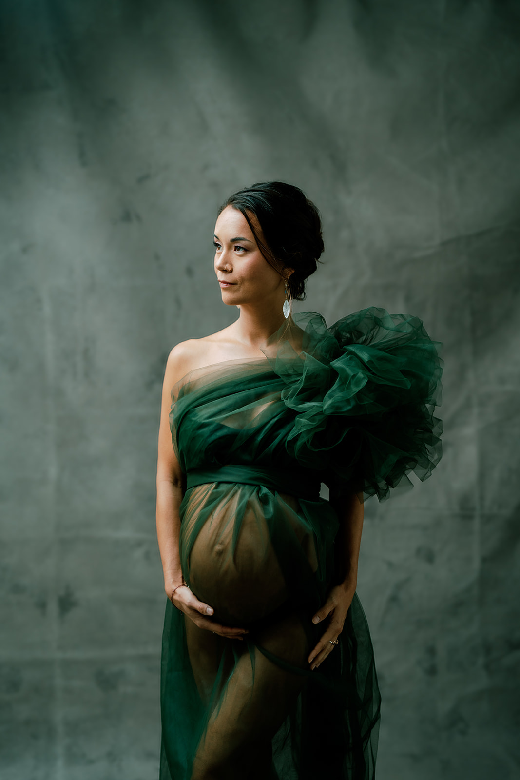A pregnant woman in an emerald gown posing for a photo.