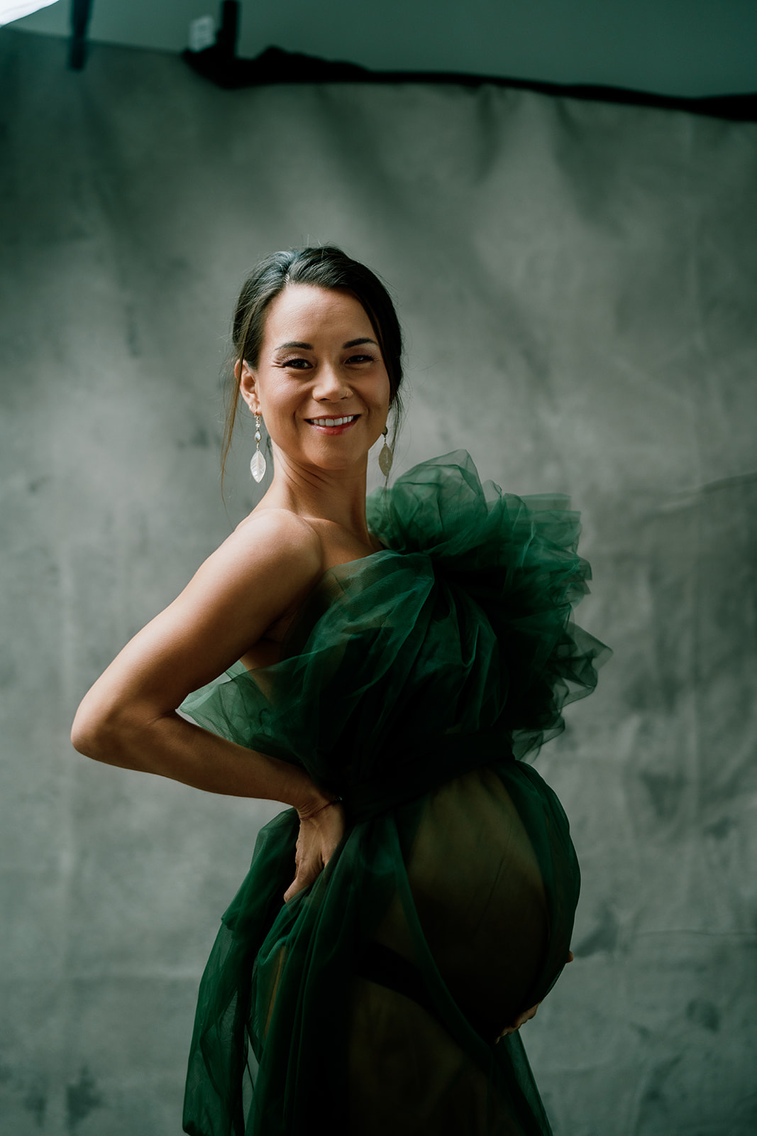 A pregnant woman smiling towards the camera in a green dress posing for a photo.