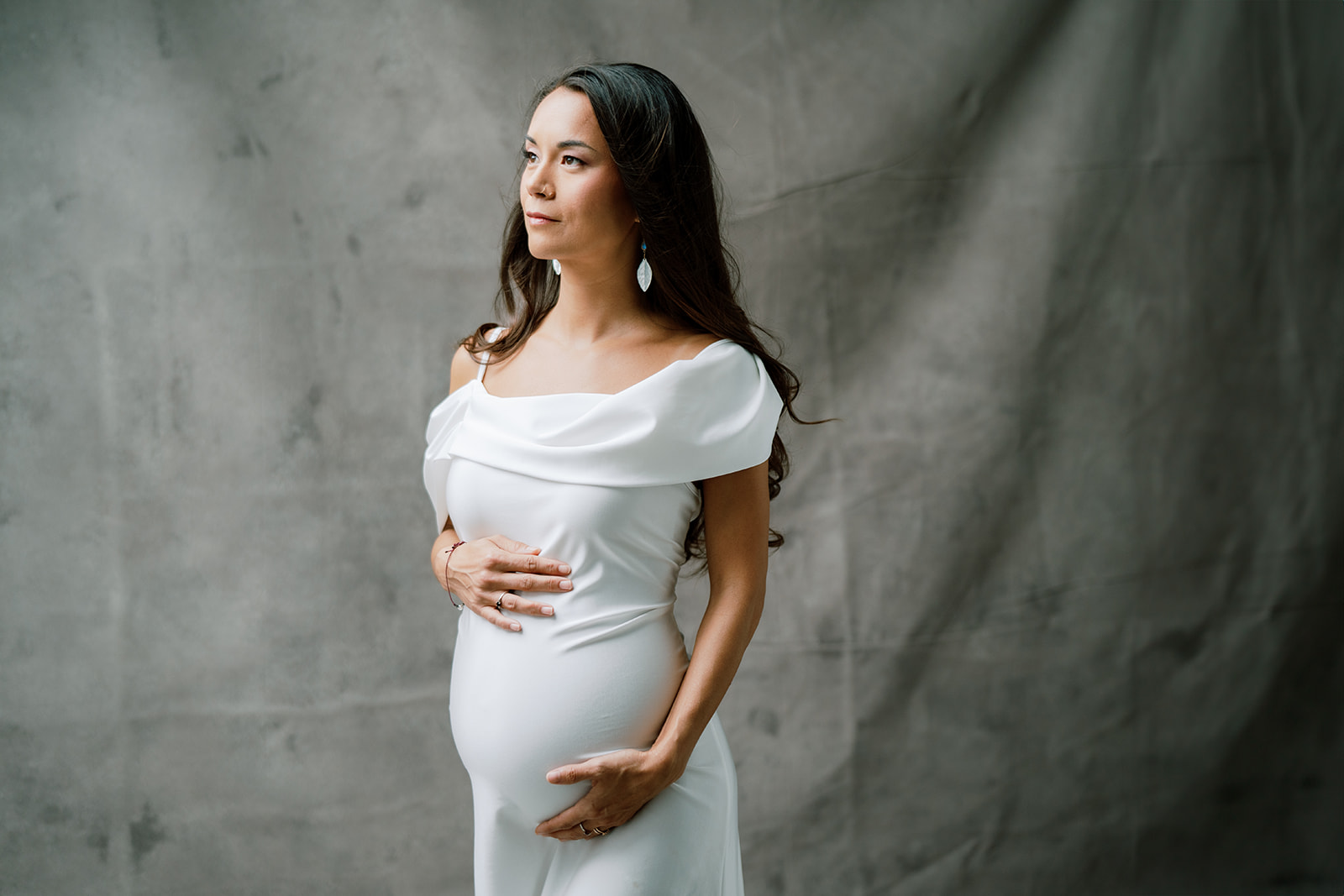 A pregnant woman in a white dress looking to the side.