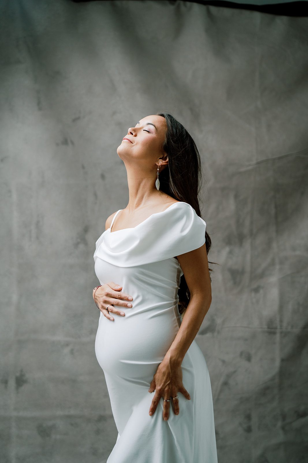 A pregnant woman in a white dress posing for maternity photography.