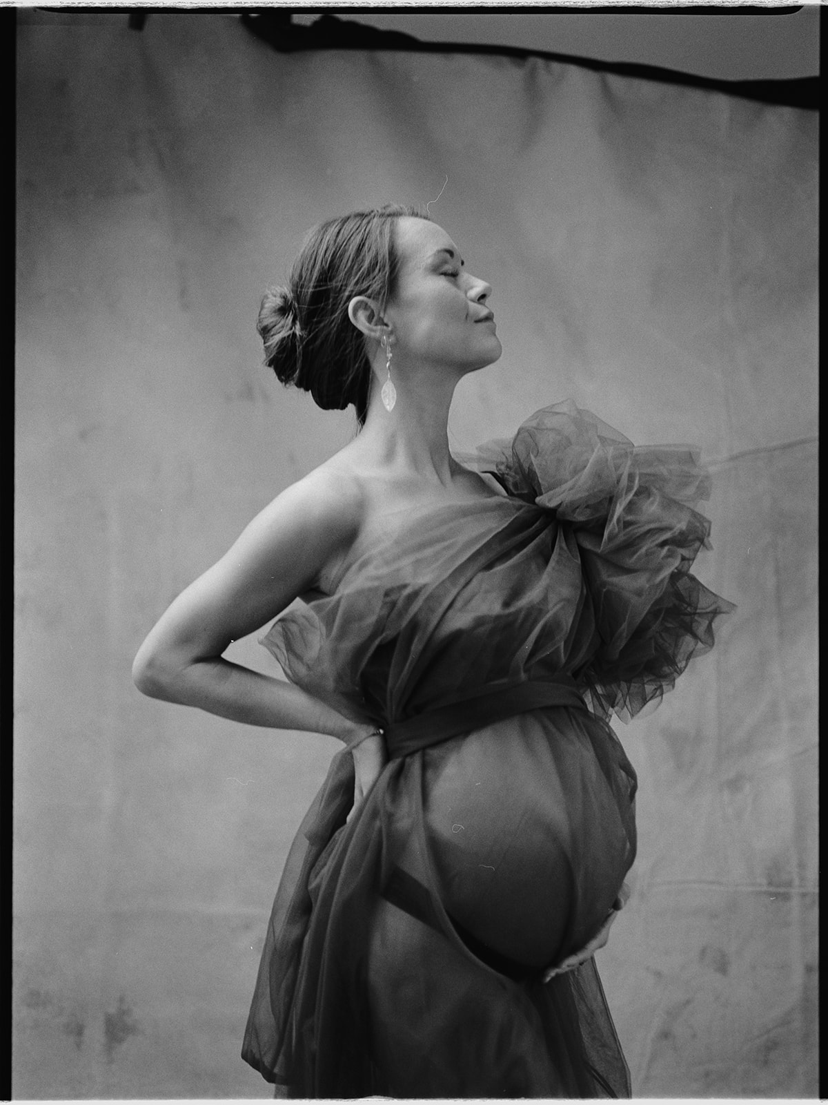 A pregnant woman leaning to the right with her hand on her waist in a black and white photo.