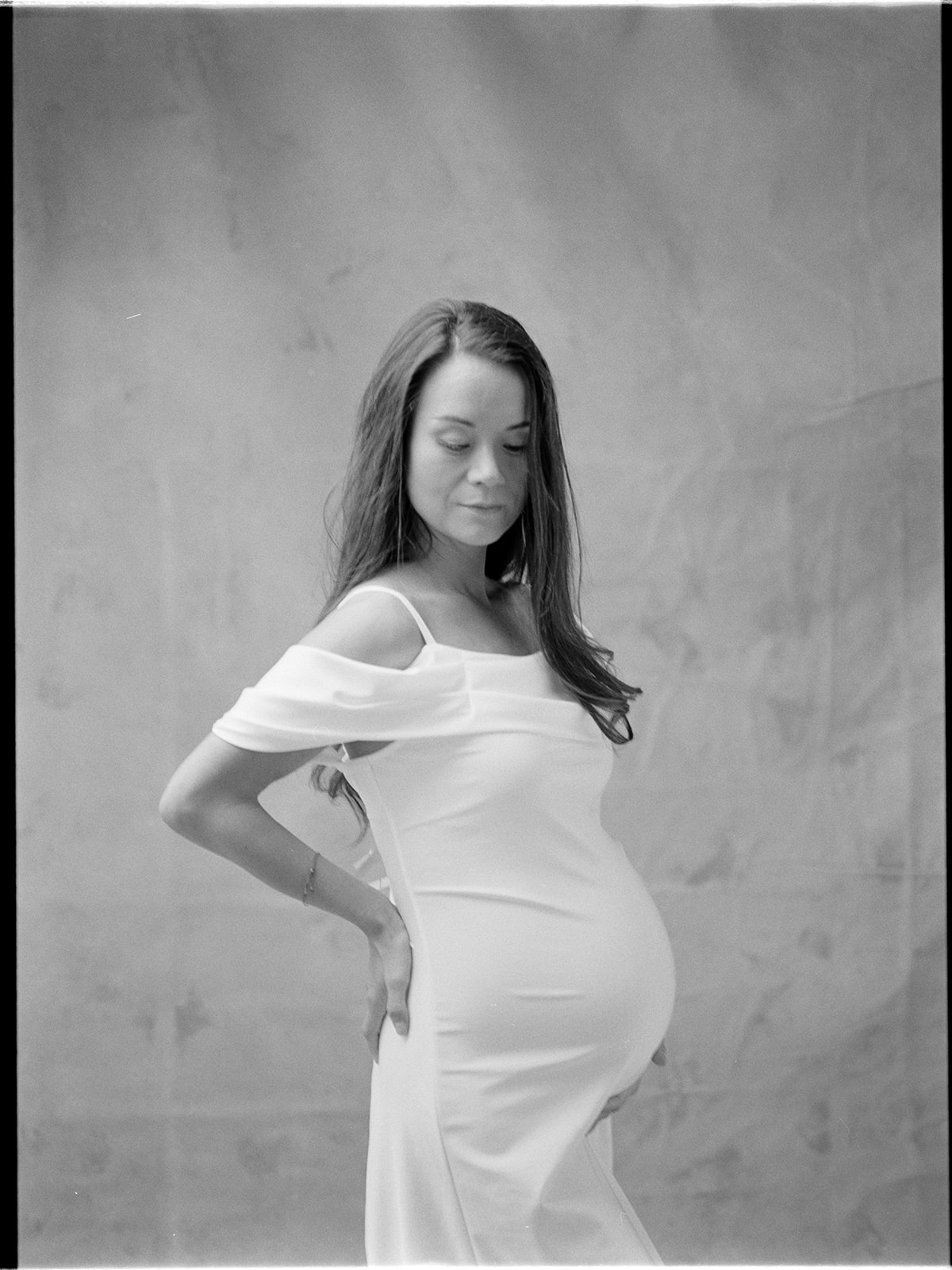 A pregnant woman in a white dress, captured in a black and white photo.