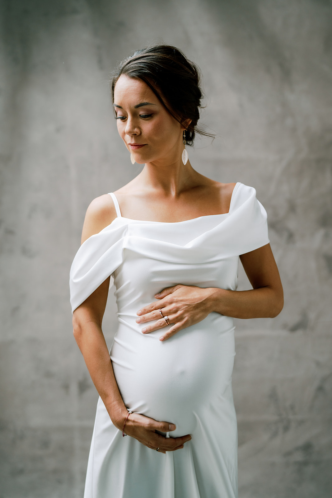 A pregnant woman in a white dress with her hair tied up posing for a photo.