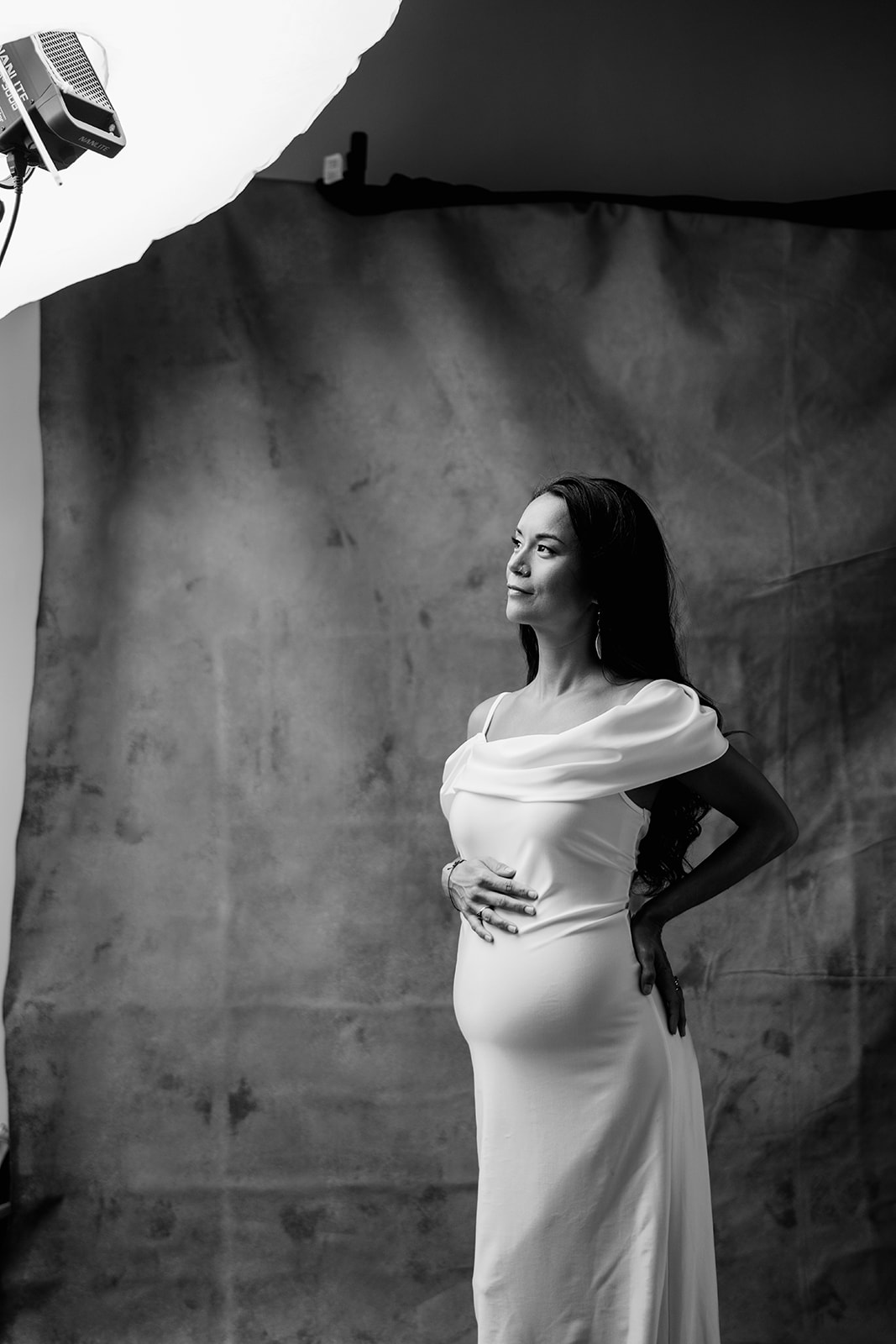 A monochrome photo of a pregnant woman in a white dress touching her bump.