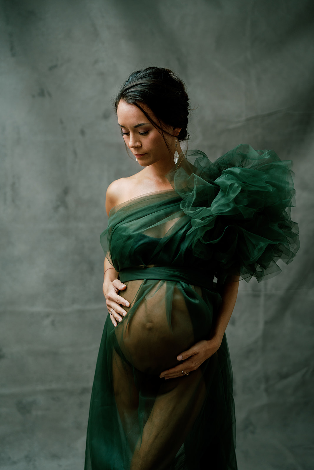 A pregnant woman in a green gown looking down posing for a photo in her maternity session.