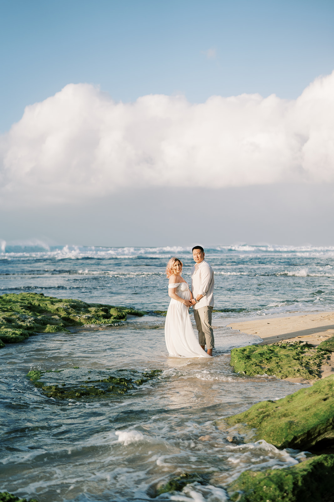 Couple holding hands looking at each other on a beach  Maternity session captured by Megan Moura Oahu Photographer