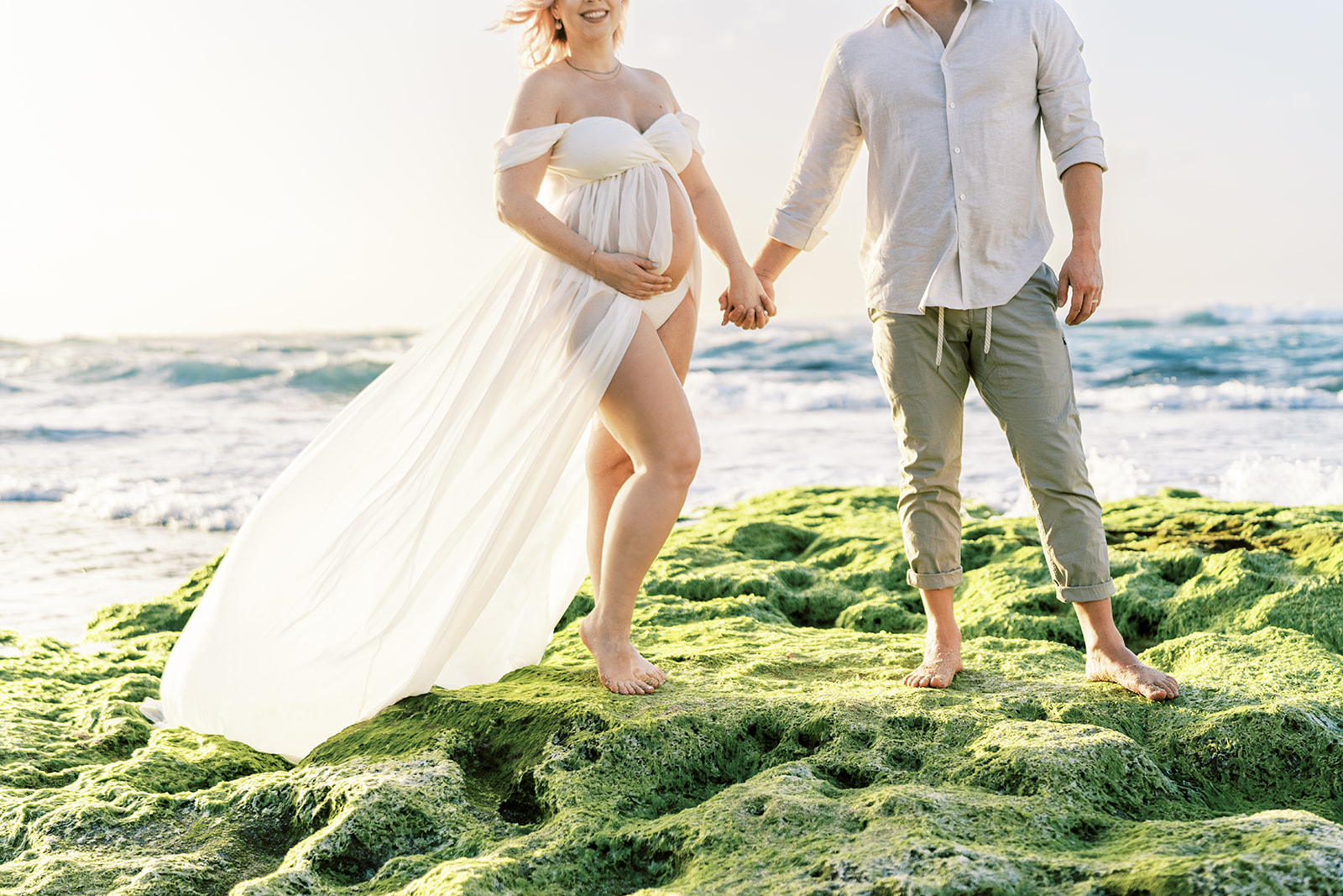 Couple holding hands on a beach with waves in the background Maternity session captured by Megan Moura Oahu Photographer