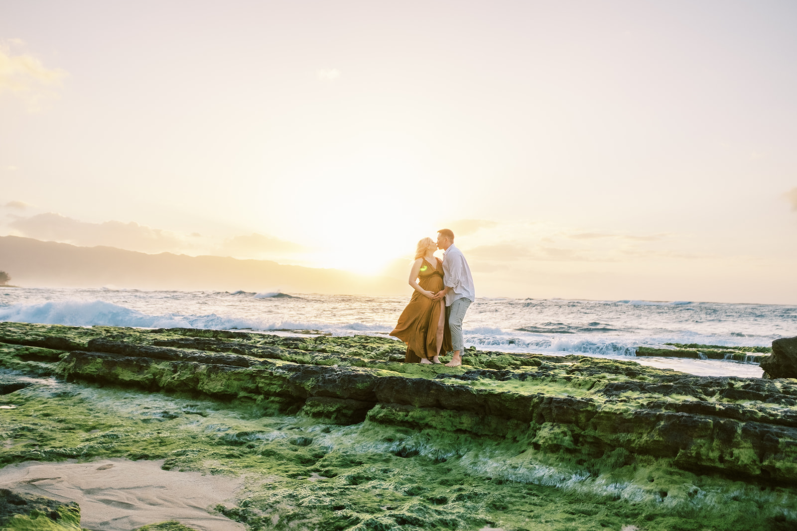 Couple sharing a romantic moment on a rocky beach at sunset on Oahu captured by Megan Moura