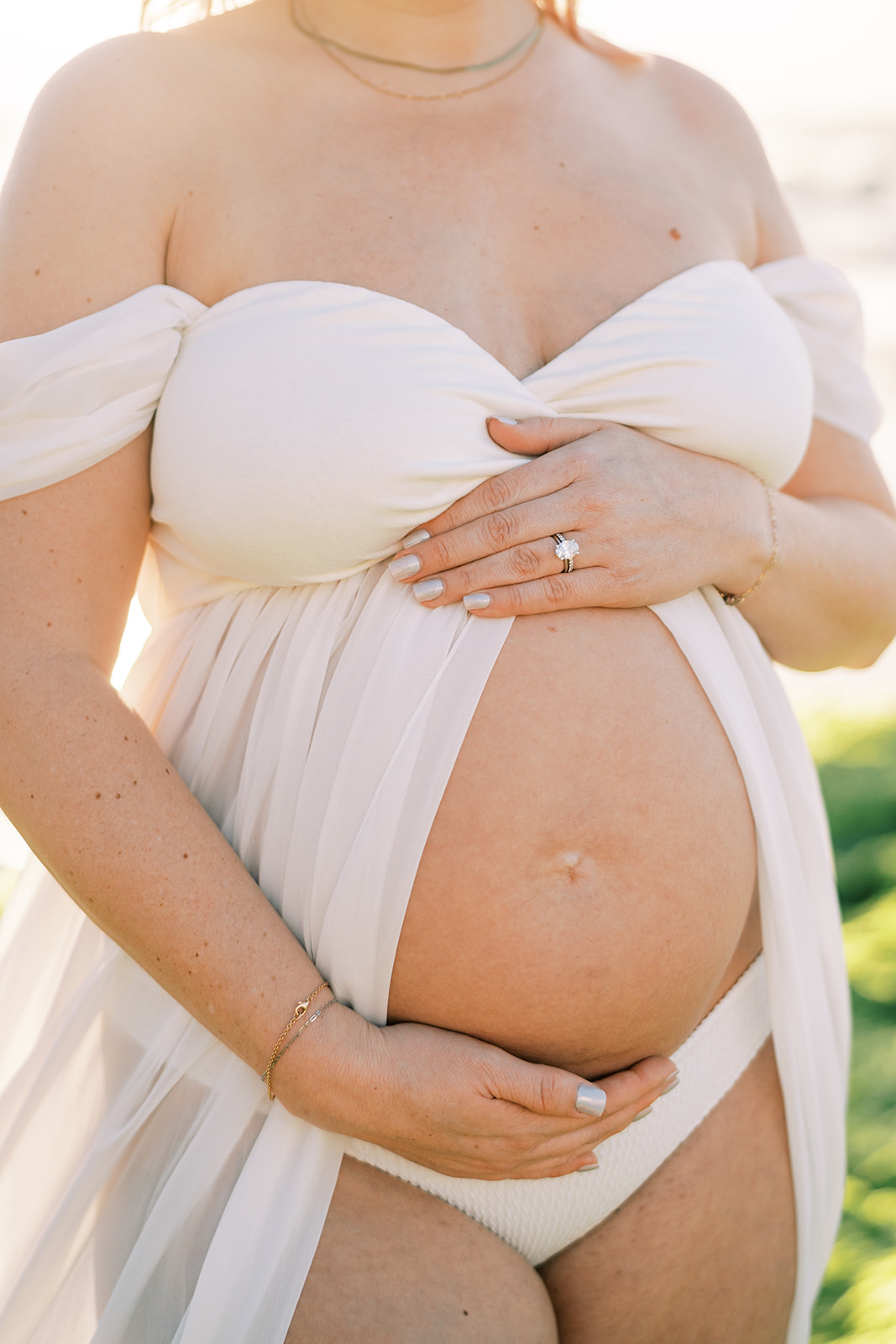 Close up photo of a baby bump cradled by the mom-to-be in white lace dress Maternity session captured by Megan Moura