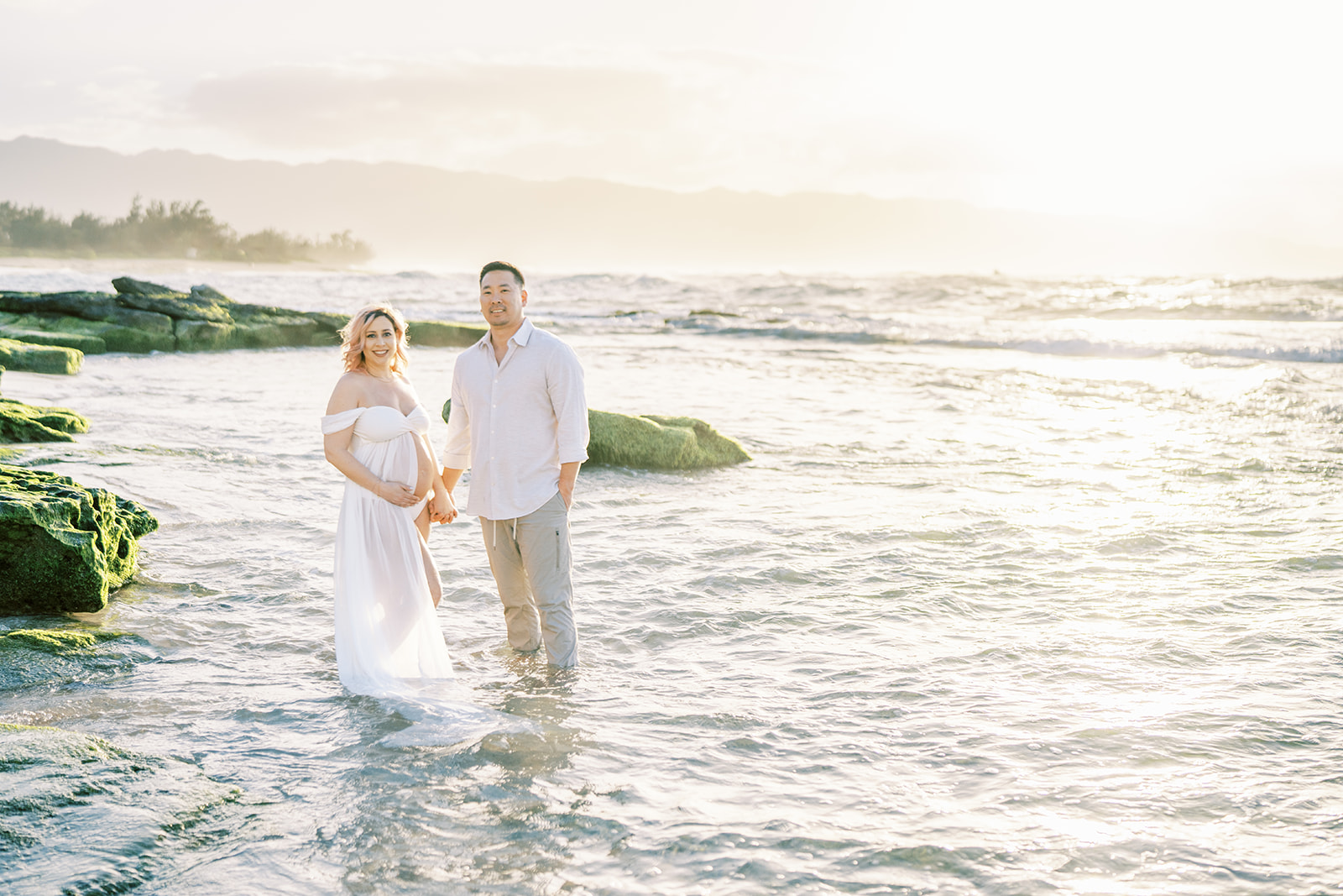 A couple holding hands looking ahead during their Maternity Session with Megan Moura on Oahu beach during sunset.