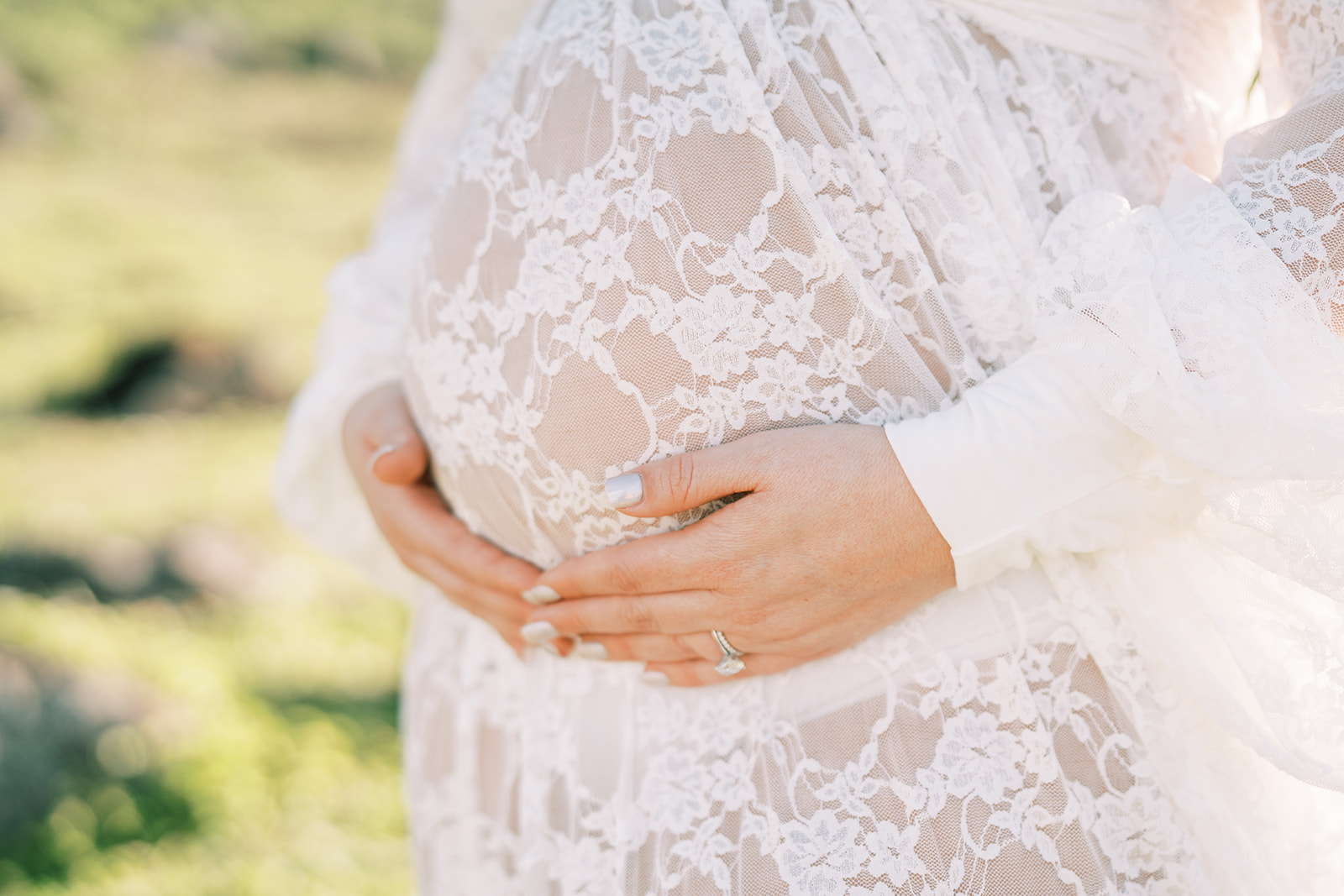 Pregnant woman in a beautiful maternity outfit holding her belly tenderly outdoors.
