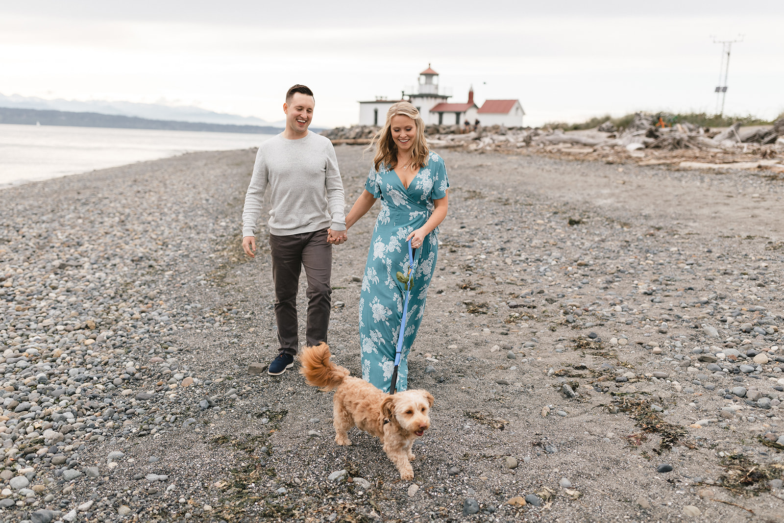 Engagement session at Discovery Park in Seattle with couple walking their dog on the beach.