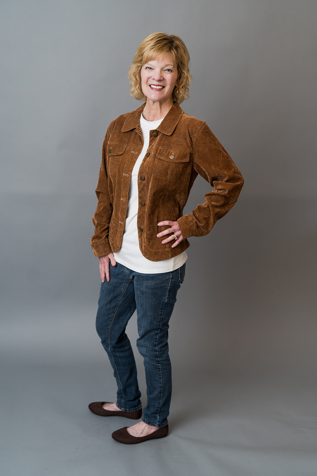 Blonde woman in jeans and a brown jacket poses for a brading session