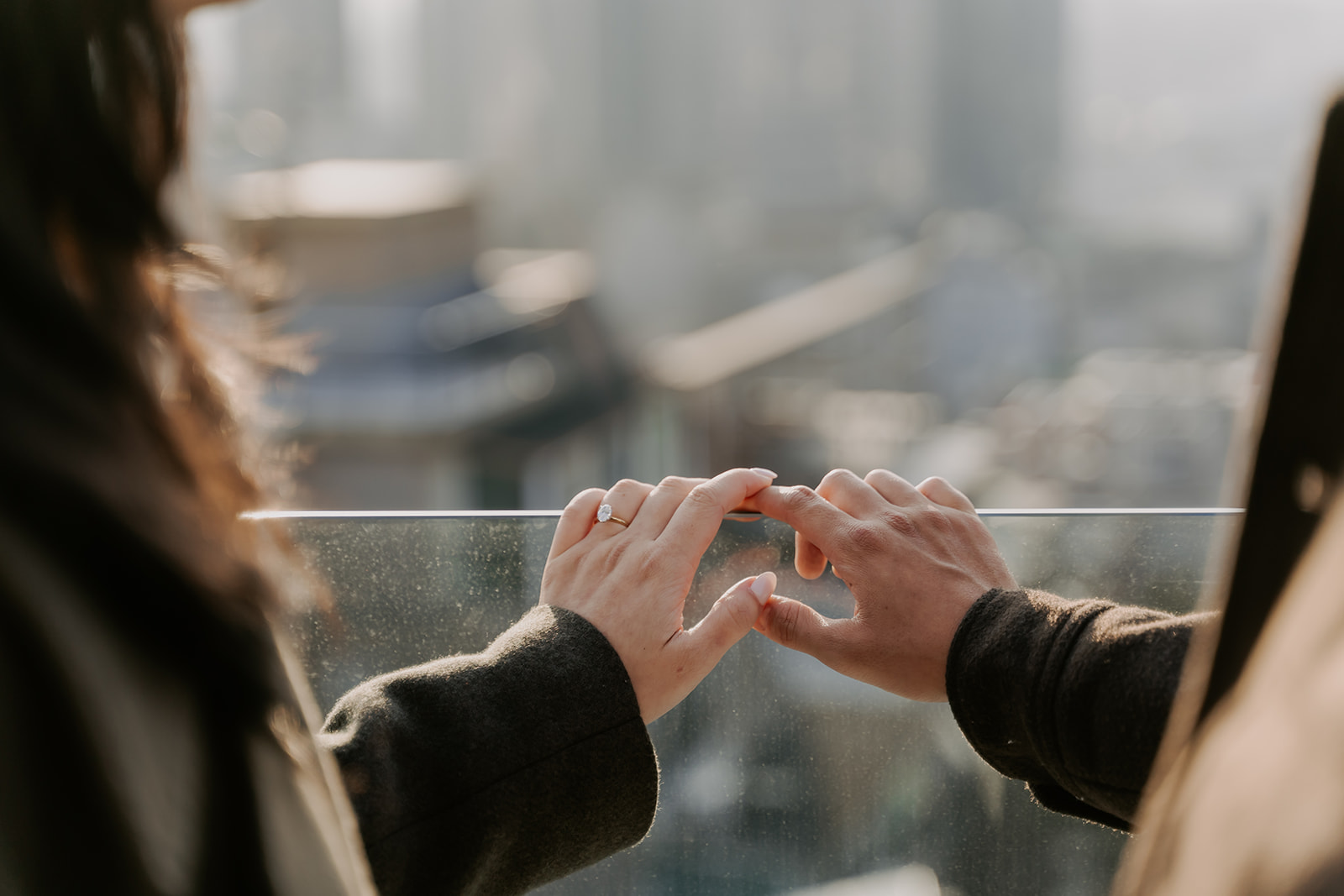 Two people holding hands, connecting with their fingers against a view of Seoul.
