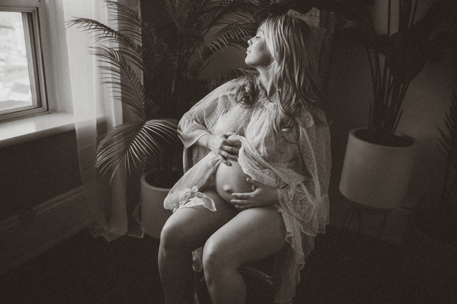 Black and white moody maternity picture of soon to be mom holding her baby bump