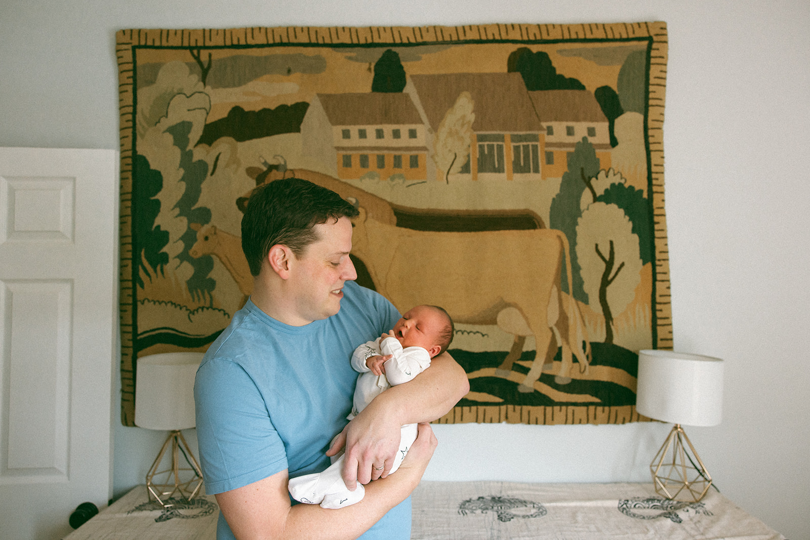 photo of new dad holding newborn daughter in front of heirloom tapestry