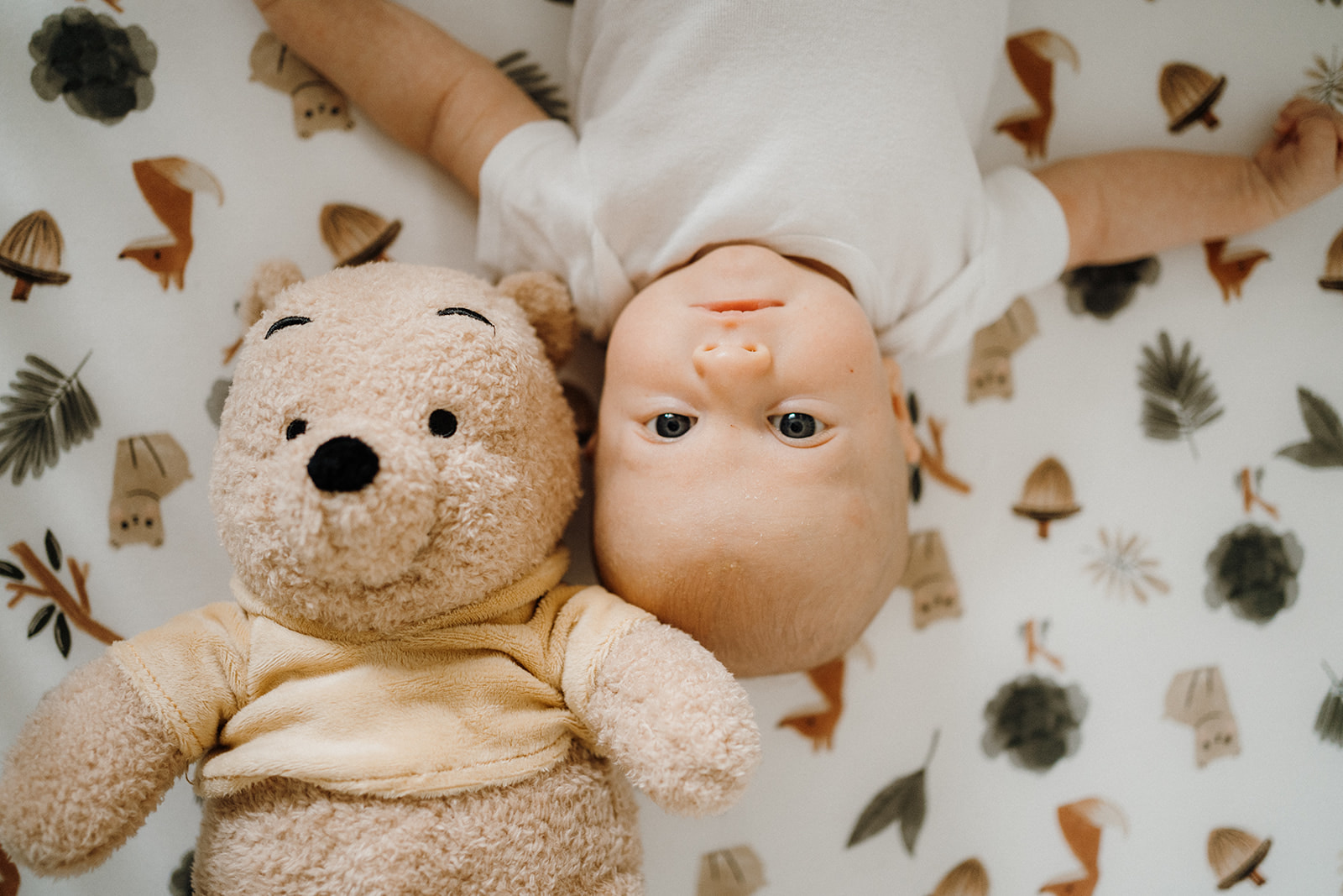 Newborn lying on their back with a teddy bear by their head.