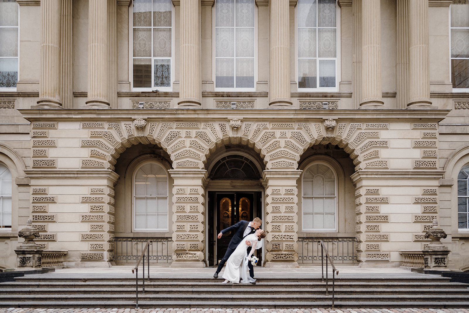 A bride and groom standing at the stairs in front of a building.