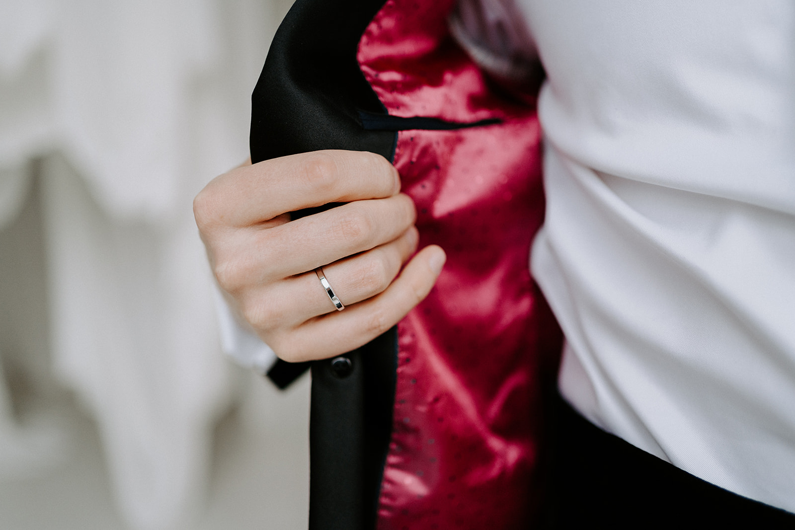 A ring on the grooms finger holding his jacket open.