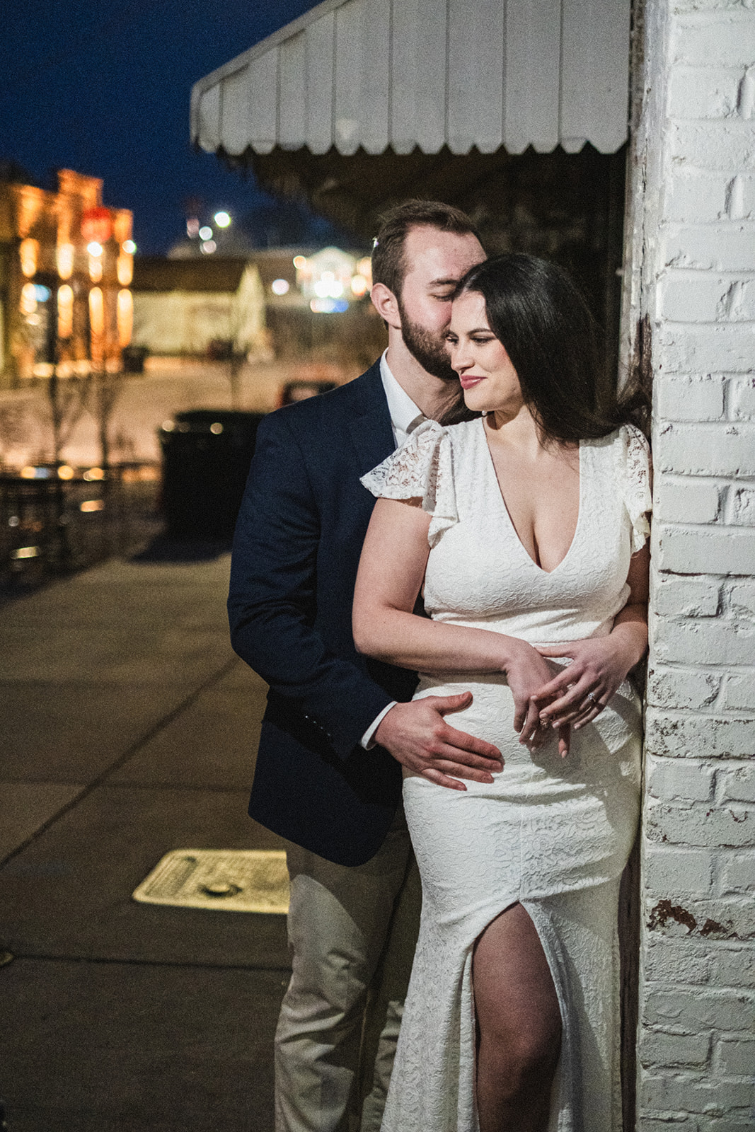 A cold and late evening engagement session with a couple snuggling together against a white wall in downtown Opelika Al.