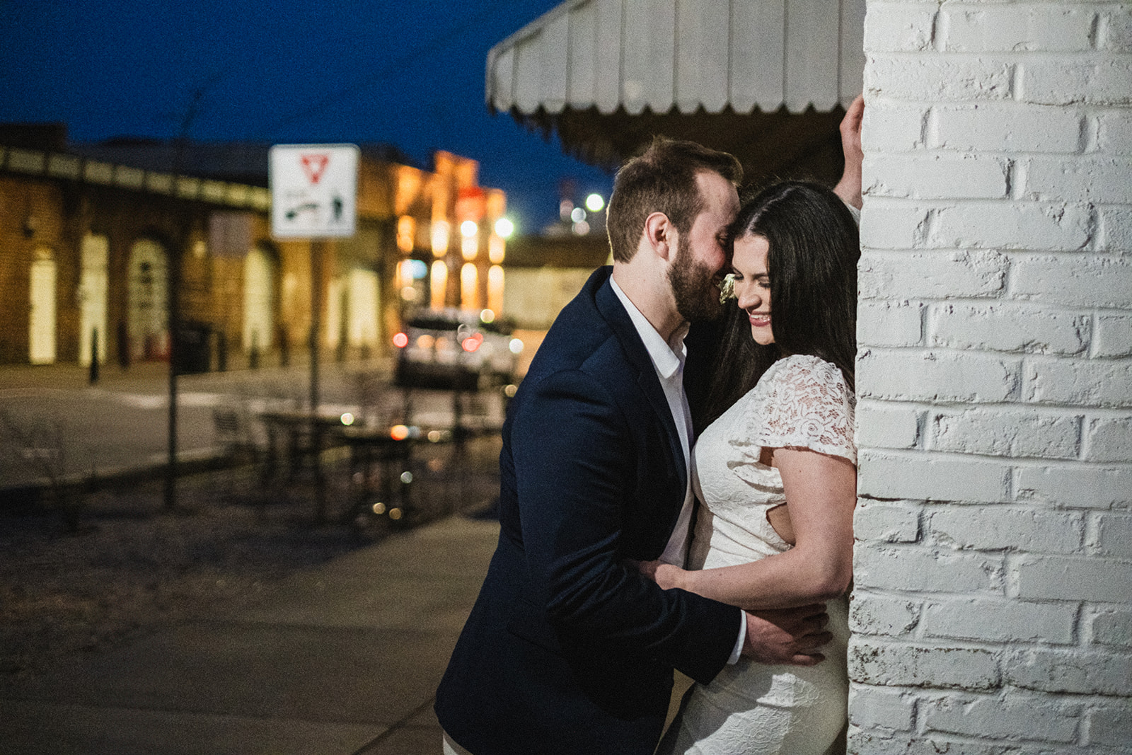 an engaged couple embracing at night against a wall in downtown opelika