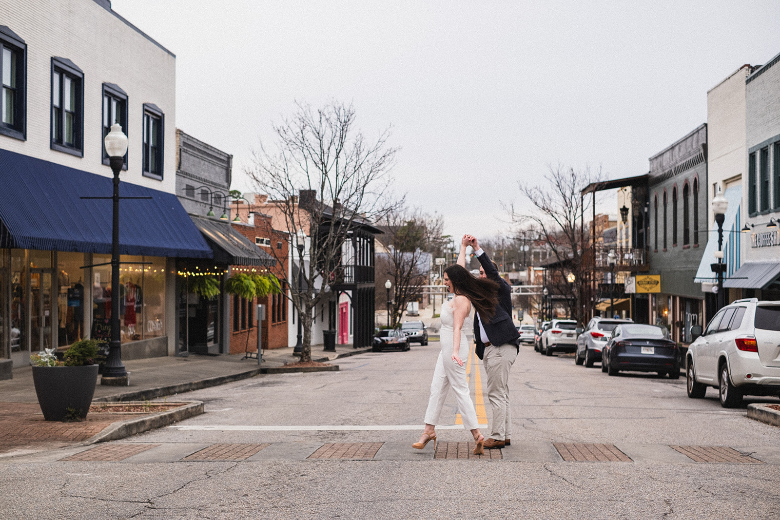 engagement session photo of a couple crossing the road while he twirls her around having a good time