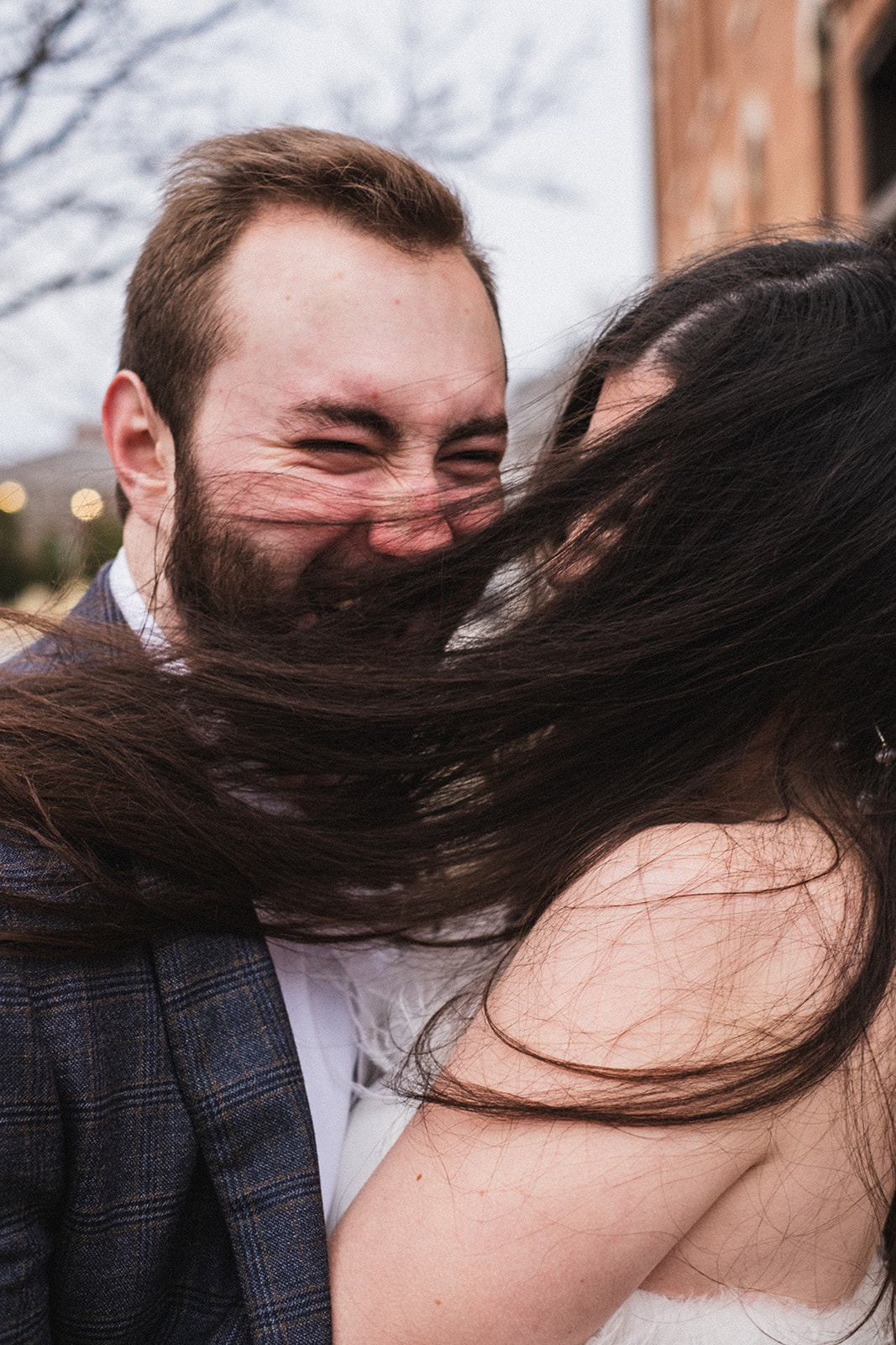 hair blown across both of their faces while taking engagement photos