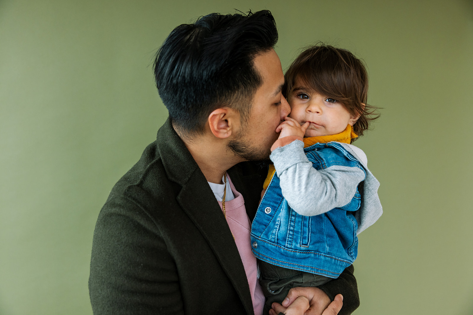 dad holding and kissing toddler against green background