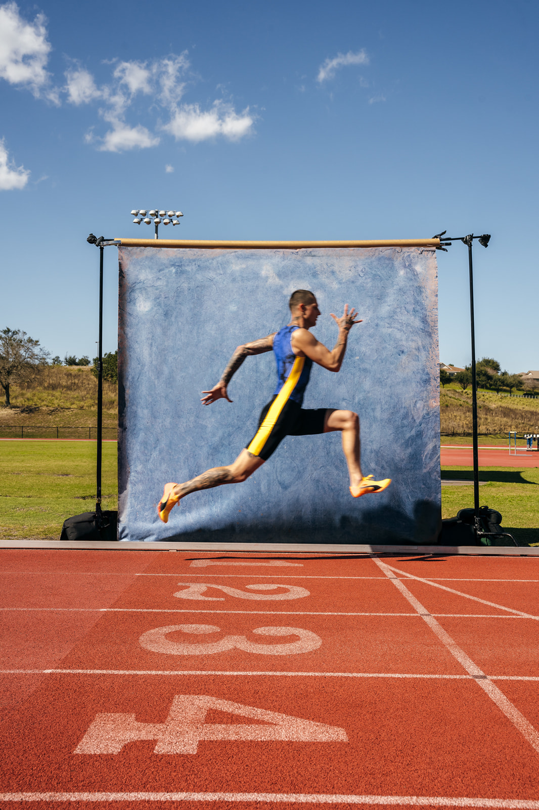 Nick Mayhugh runs on a track with a blue, hand painted canvas backdrop by Ultraviolet Backdrop. 
