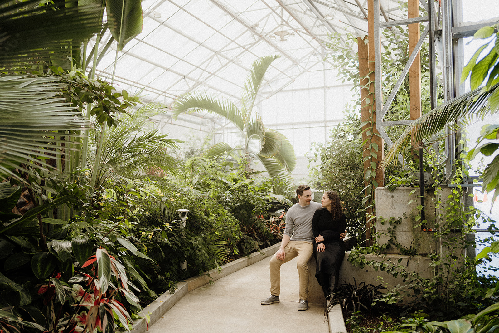 A man and a woman sitting down in a greenhouse.