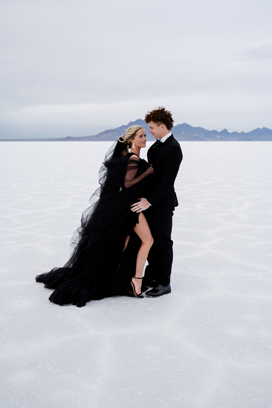 Black tux and black dress with black tulle veil stands out in Salt Flats Utah wedding photography.